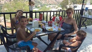 Una familia cenando en un porche cubierto con vistas a un paisaje montañoso.