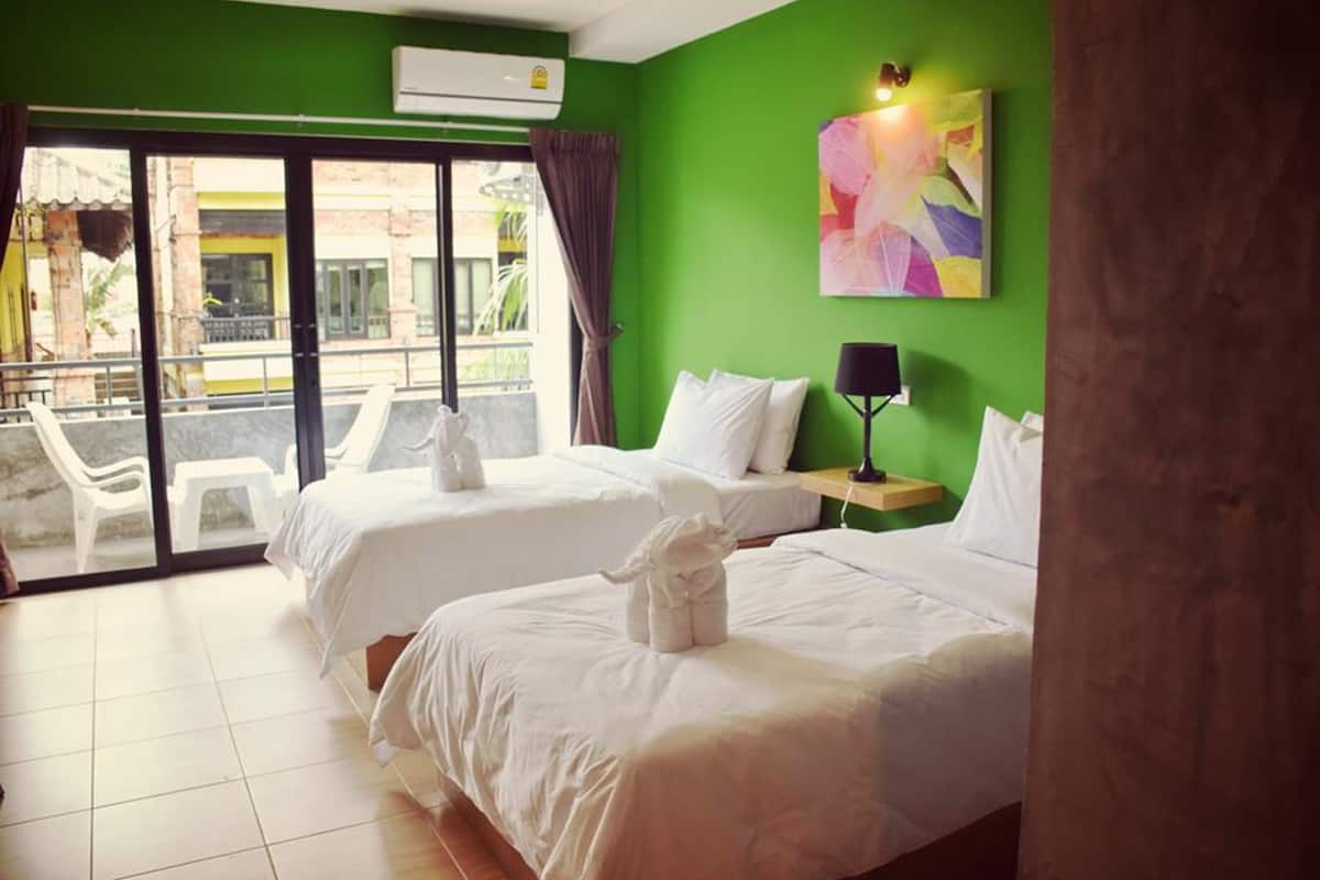 A hotel room with two beds, a green wall, a painting, and a view of the outside.
