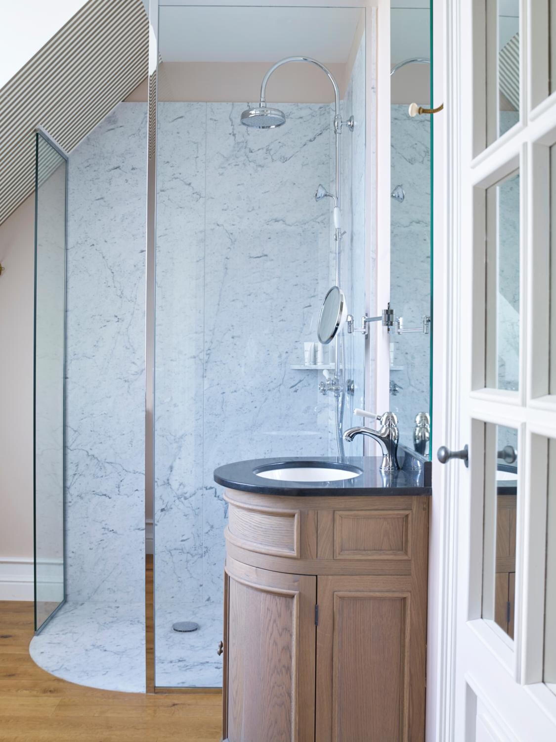 Un baño moderno con ducha de mármol, lavamanos con espejo y armarios de madera.