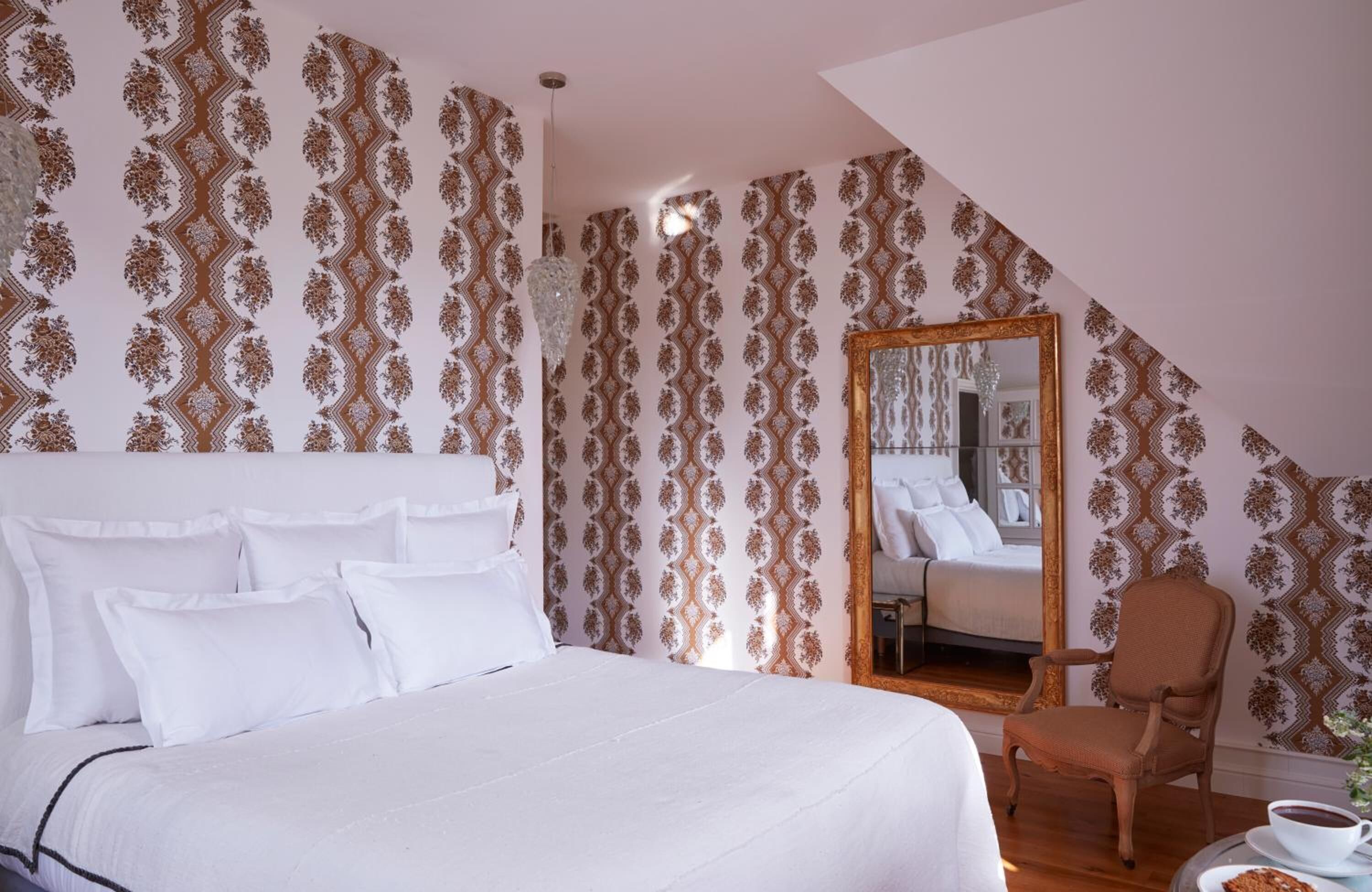 Un dormitorio con una cama grande, una silla, un espejo y una taza sobre una mesa.
