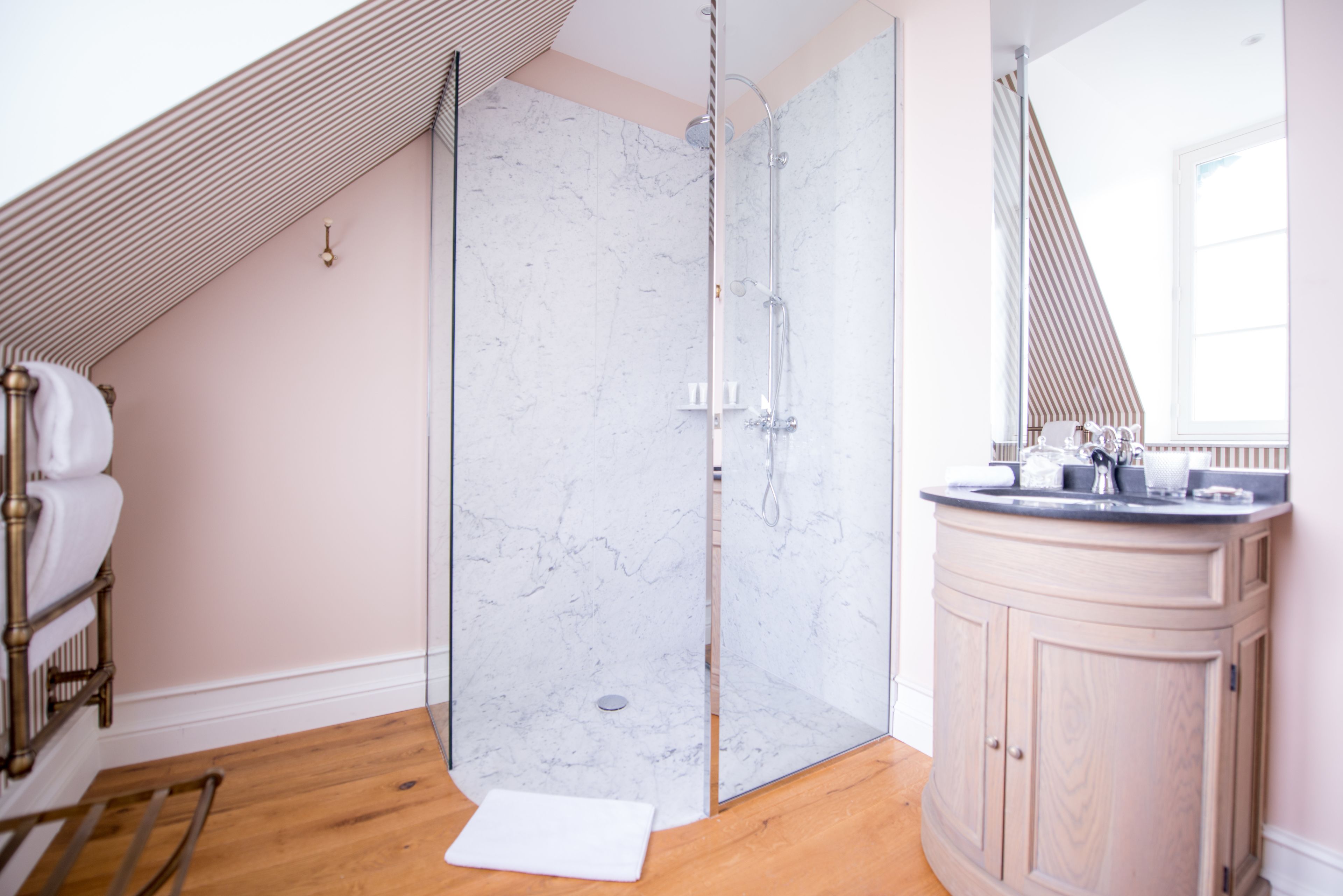 A modern bathroom with a glass shower enclosure, a wooden floor, a vanity with a mirror, and a towel rack.