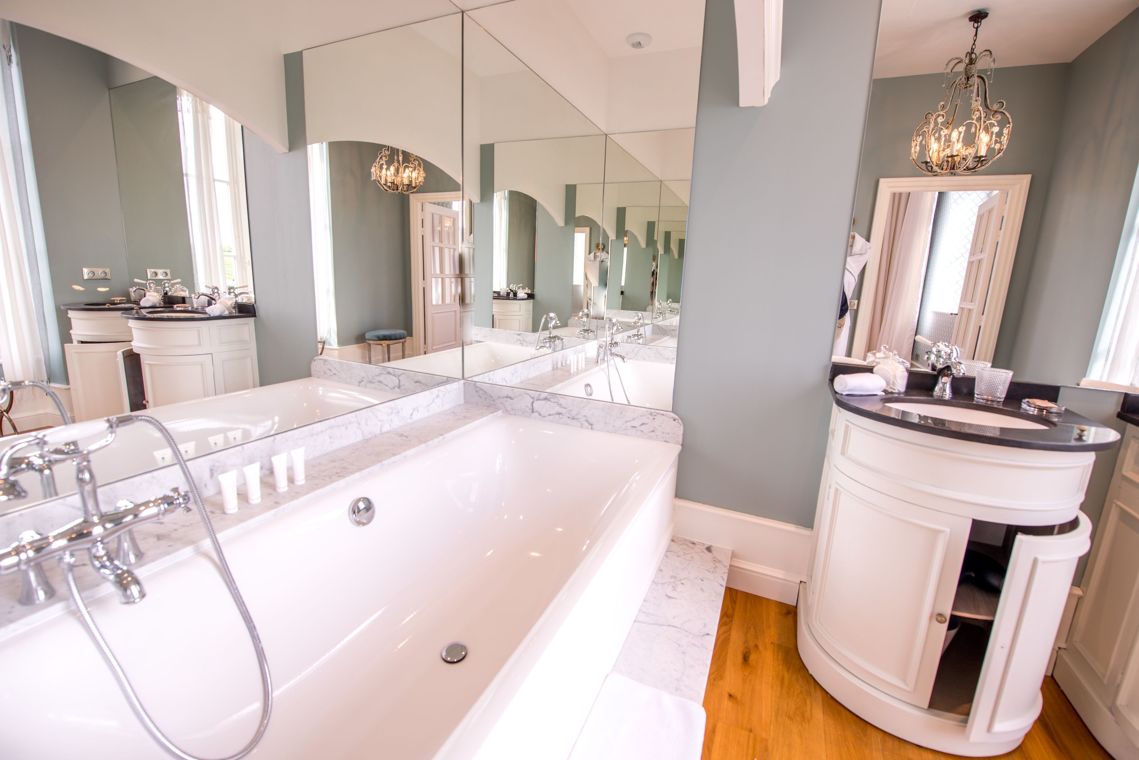 A modern bathroom with a large bathtub, a vanity with a mirror, and a chandelier.
