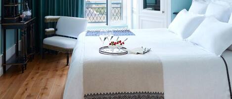 A bedroom with a bed, a chair, a table with a tray of items, a chandelier, and a view of the outdoors.