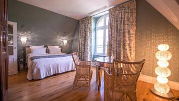 A bedroom with a bed, two chairs, a table, a lamp, and a window with curtains.