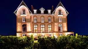 A large, illuminated building with multiple windows and balconies, surrounded by greenery. - Château de Sacy (Sacy)