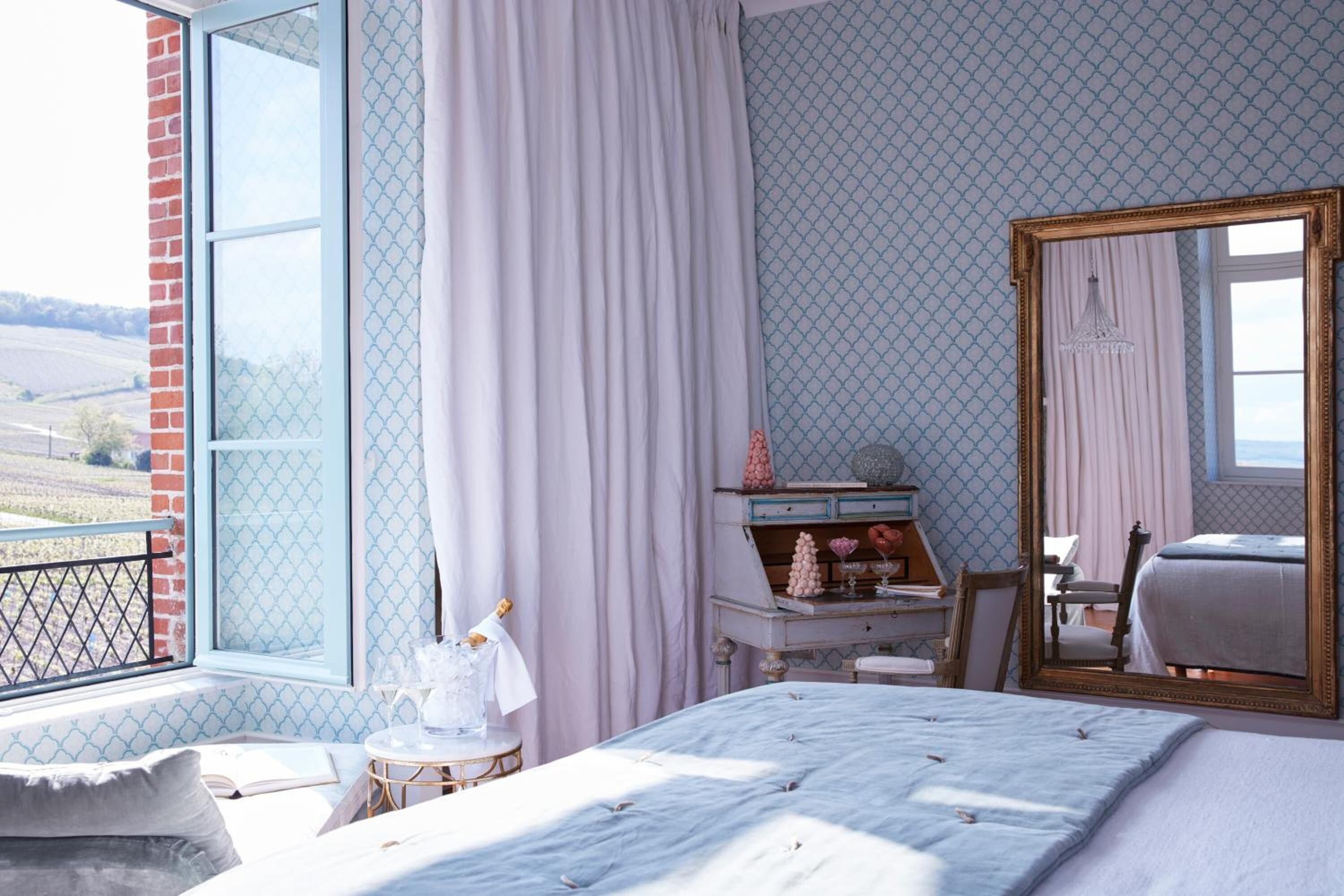 A bedroom with a large window, a bed, a dresser, and a mirror.