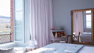 A bedroom with a large window, a bed, a dresser, and a mirror.