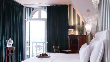 Une chambre à coucher avec un grand lit, une table de chevet en verre, un lustre et une vue sur l’extérieur.