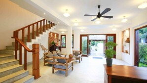 Amplia sala de estar con escalera de madera, asientos cómodos, ventilador de techo y vistas al exterior.