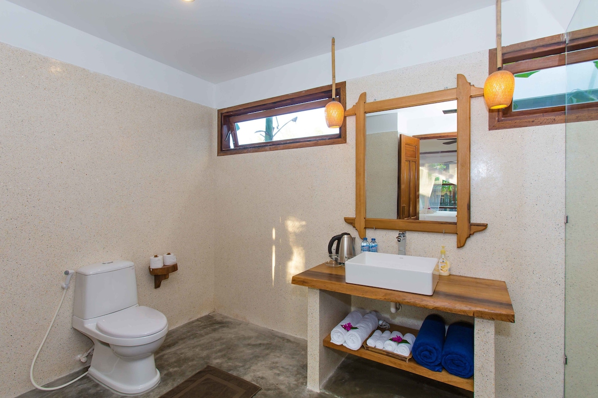 A bathroom with a toilet, a sink, a mirror, and a shelf with towels.