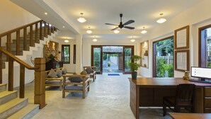 Un interior espacioso con una escalera, muebles de madera, un escritorio con computadora y grandes ventanales que ofrecen vistas al exterior.