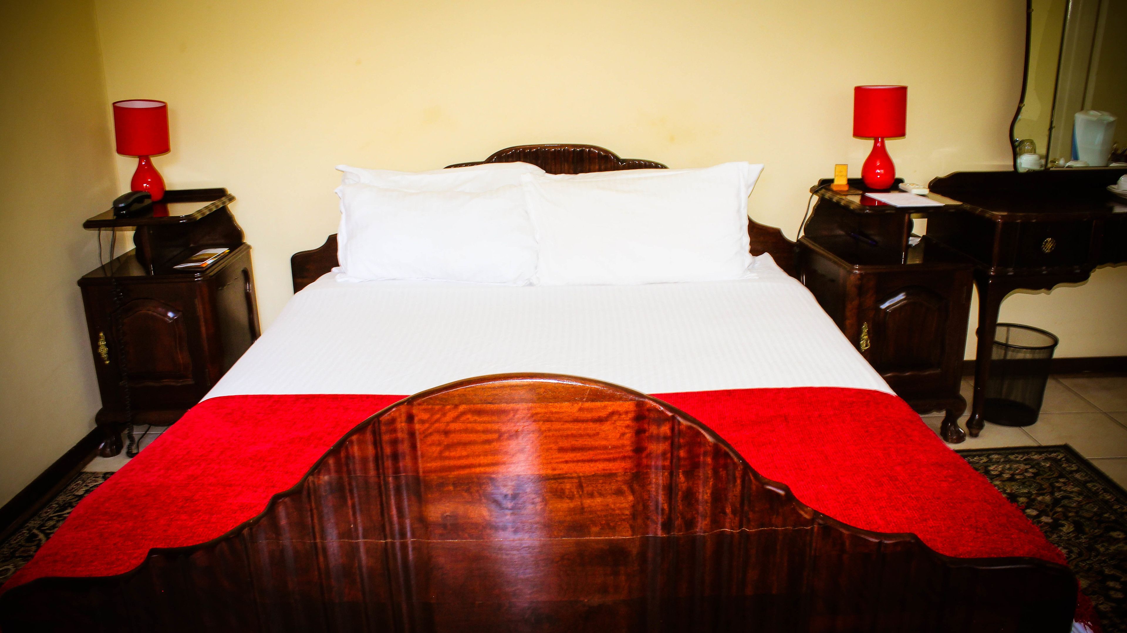 Una cama bien hecha con cabecera de madera, dos mesitas de noche con lámparas y un plaid rojo sobre la cama.