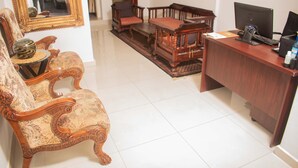 Un comptoir d’accueil traditionnel en bois, équipé d’un ordinateur et d’un téléphone. On y trouve un fauteuil à motifs et un banc en bois avec des coussins. Un grand miroir est accroché au mur.