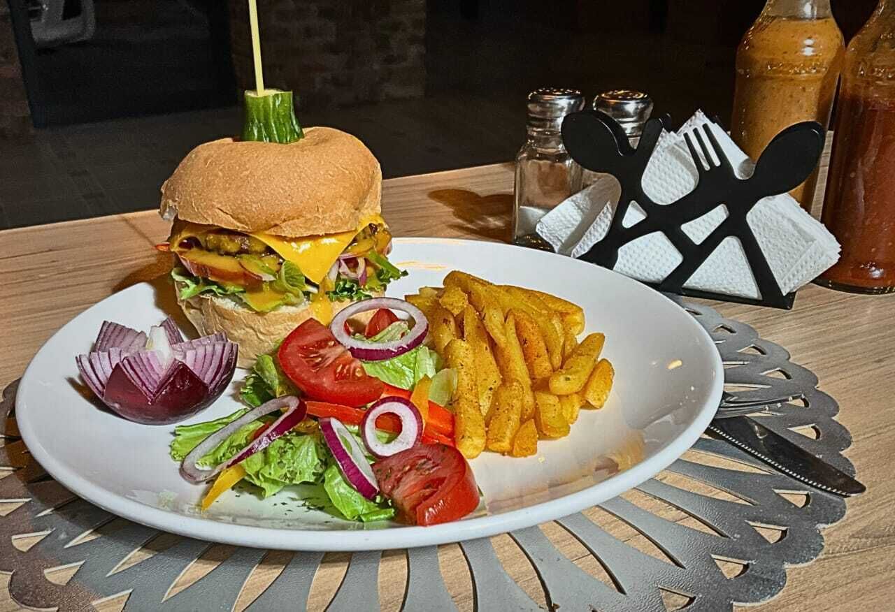 Un plato con una hamburguesa, papas fritas y una ensalada sobre una mesa con un mantel individual.