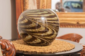 A decorative glass vase with a spiral pattern on a woven placemat, placed on a round table with a wooden base.