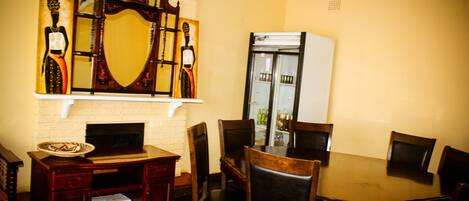 A dining area with a wooden table, six chairs, a fireplace, and a refrigerator.