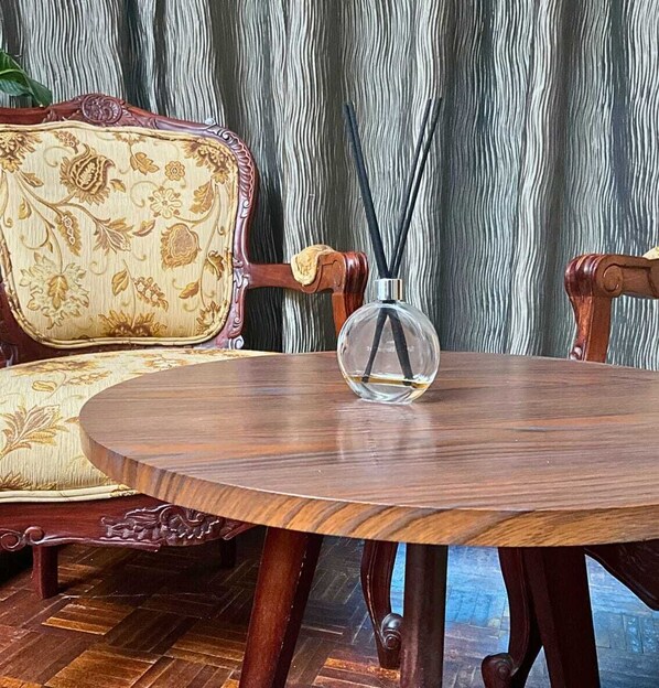 A round wooden table with a clear glass bottle and black sticks, placed in front of a patterned sofa.
