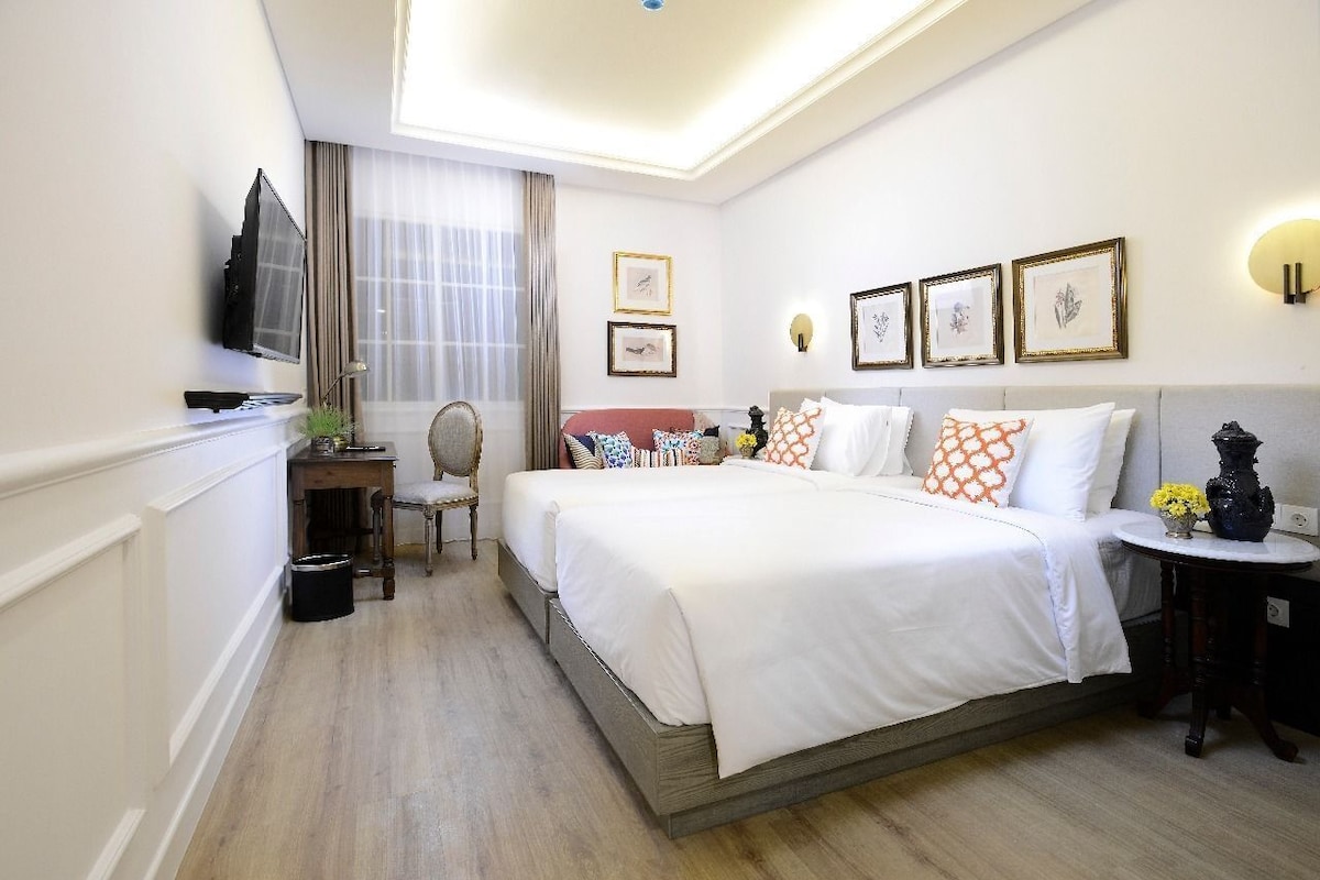 A hotel room with a large bed, a desk, a chair, a television, and framed pictures on the wall.