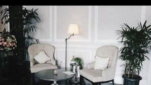 Ett rum med två fåtöljer, ett runt soffbord, en golvlampa och en krukväxt.