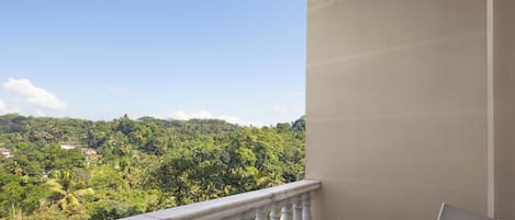Un balcón con barandilla blanca, una mesa con juego de té y una silla. Se aprecia un paisaje verde exuberante y edificios a lo lejos.