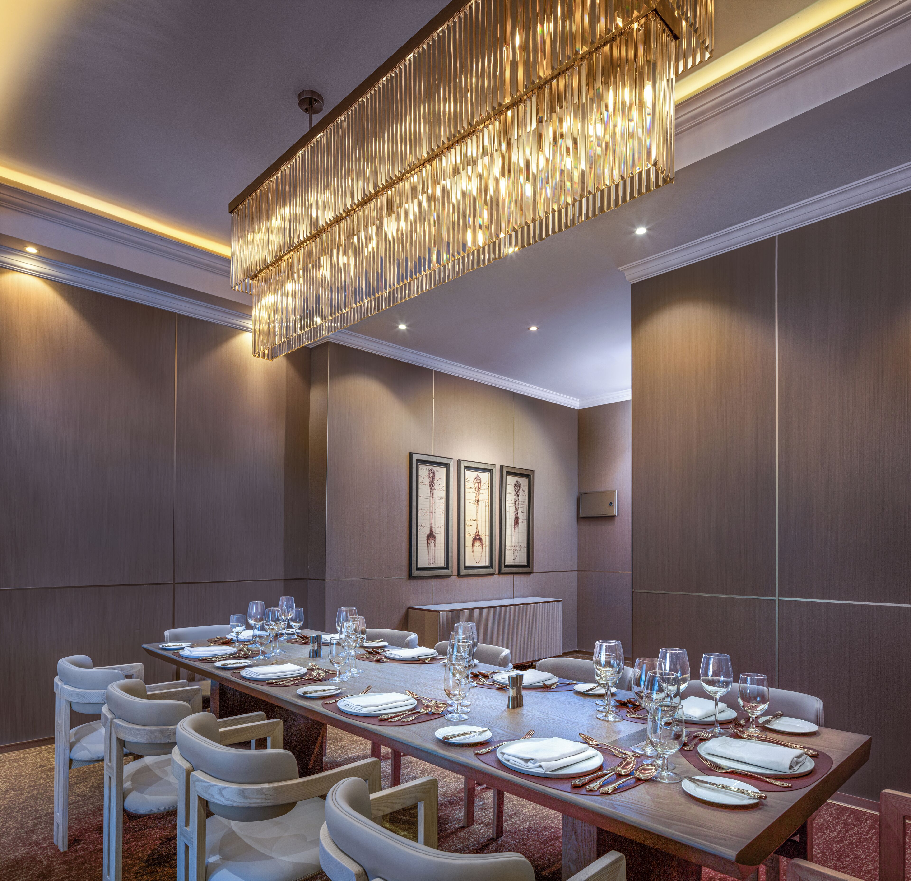 A conference room with a long table set for a meeting, framed artwork on the wall, and a modern chandelier.