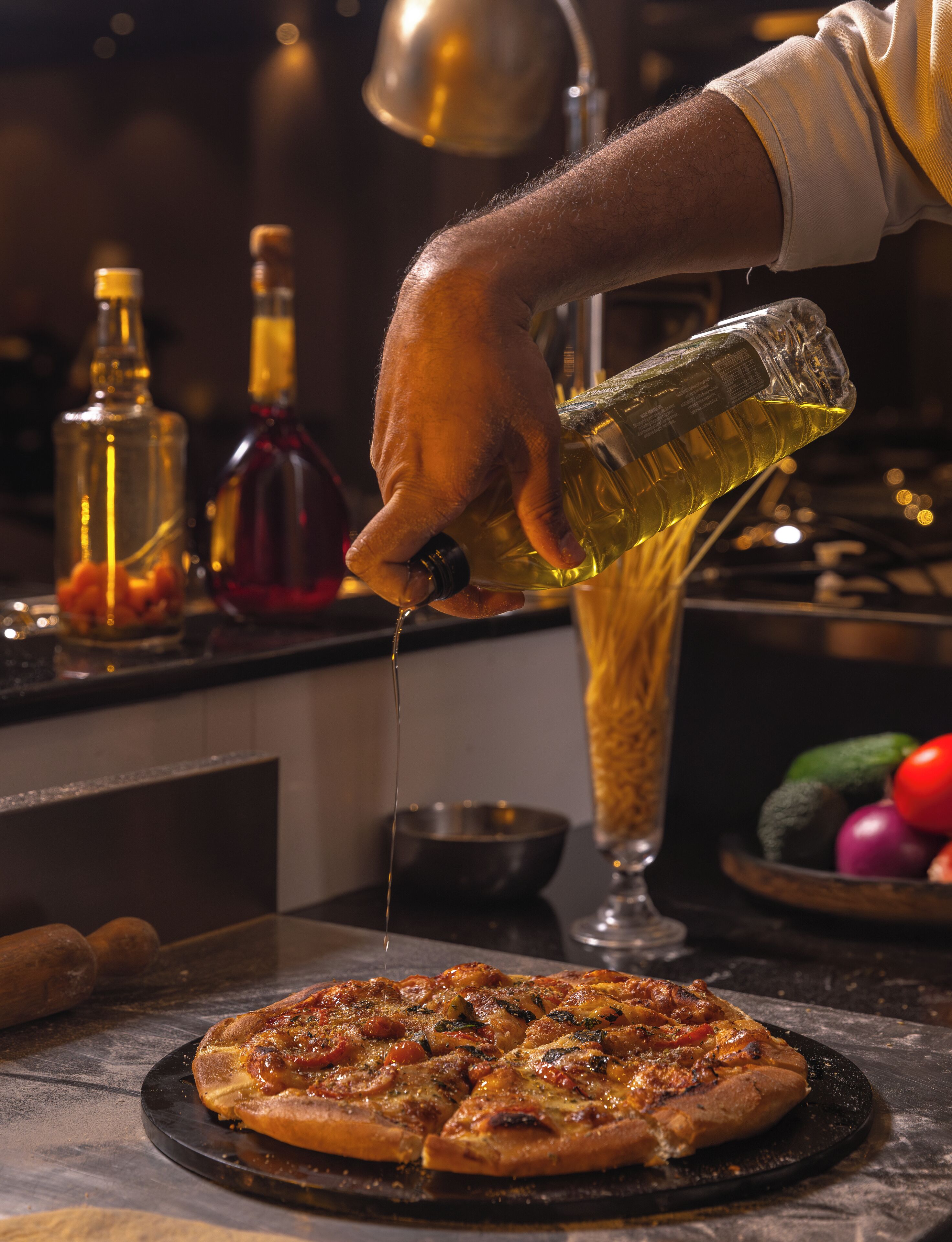 A person pouring olive oil over a pizza.