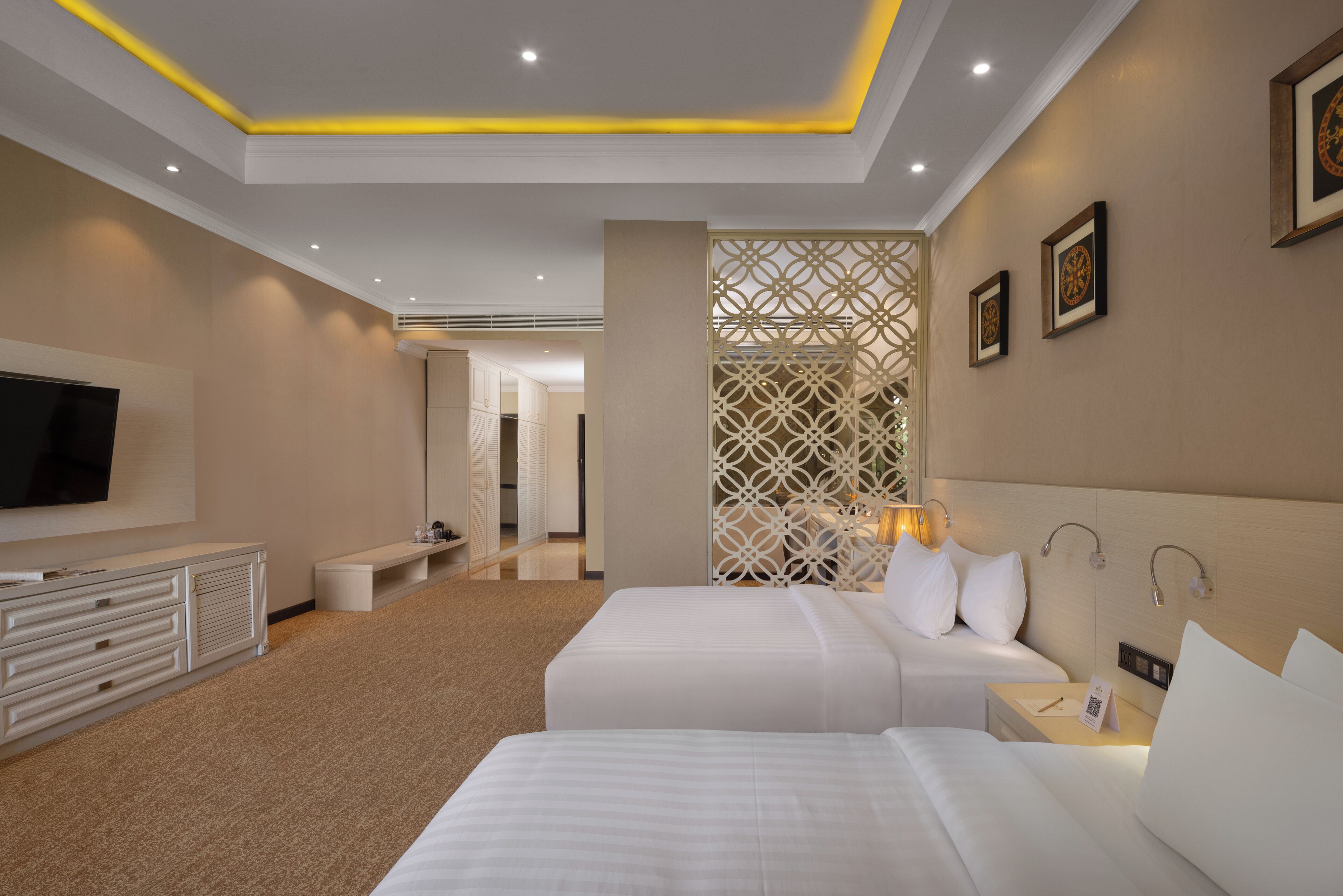 A hotel room with two beds, a TV, a desk, and a decorative partition.