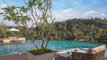 A poolside area with lounge chairs and a small table, surrounded by lush greenery and a clear blue sky.