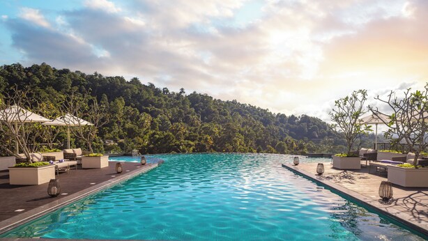 Une piscine entourée de chaises longues et de jardinières, le tout niché au pied d’une colline boisée.