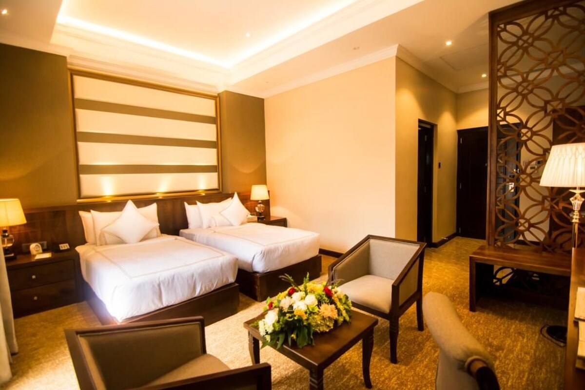 A hotel room with two beds, a sitting area with a table and chairs, and a decorative wall panel.