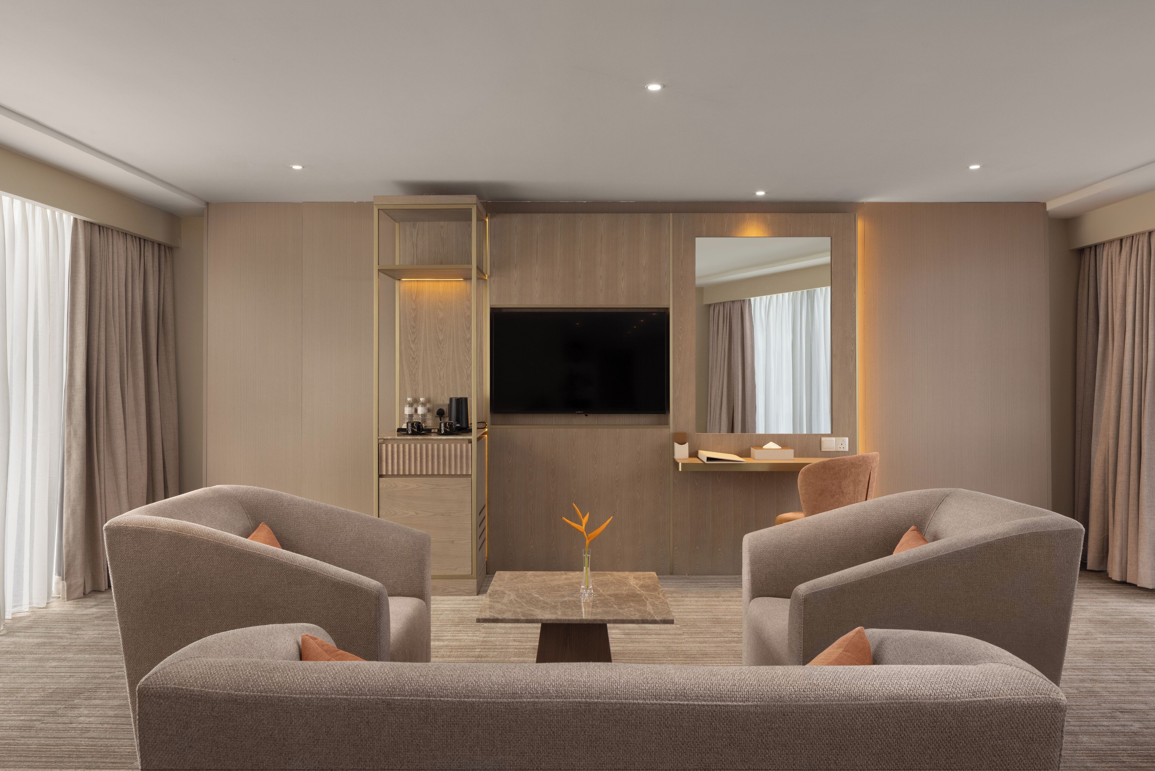 Ett modernt hotellrum med en soffgrupp, en platt-TV, ett litet bord med en vas och en spegel på väggen.