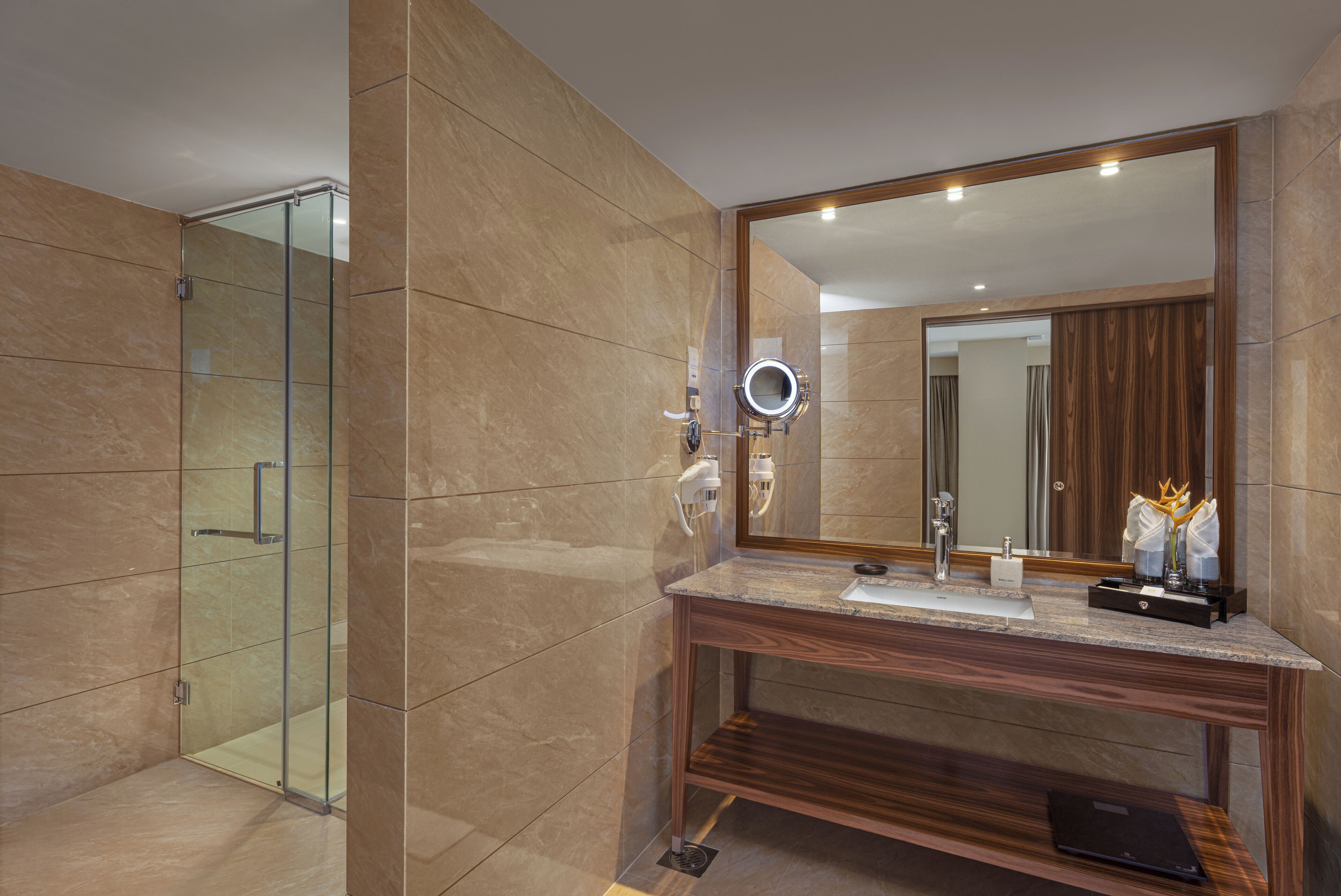 Un baño moderno con cabina de ducha de vidrio, tocador de madera y un espejo grande con luz redonda.