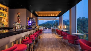 Un espace bar moderne avec un plancher en bois, des tabourets de bar rouges et une vue sur l’extérieur.