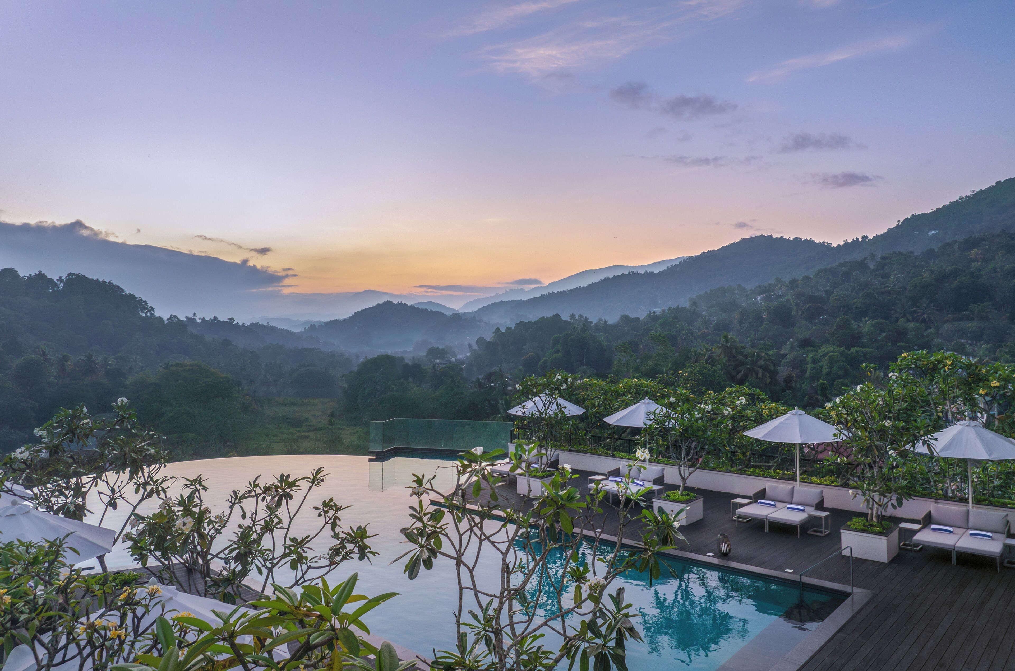 A poolside area with lounge chairs and umbrellas, surrounded by lush greenery and overlooking a valley.