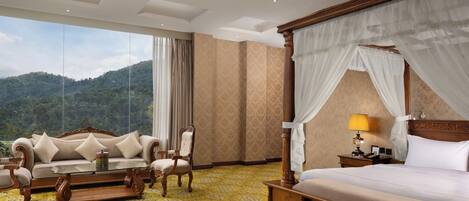 Habitación de hotel con una cama grande, un sofá, una silla, una mesita y vistas a las montañas.