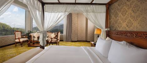 A spacious bedroom with a large bed, a sitting area with chairs, and a view of the outdoors.