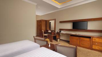A hotel room with two beds, a desk with a chair, a television, and a minibar.