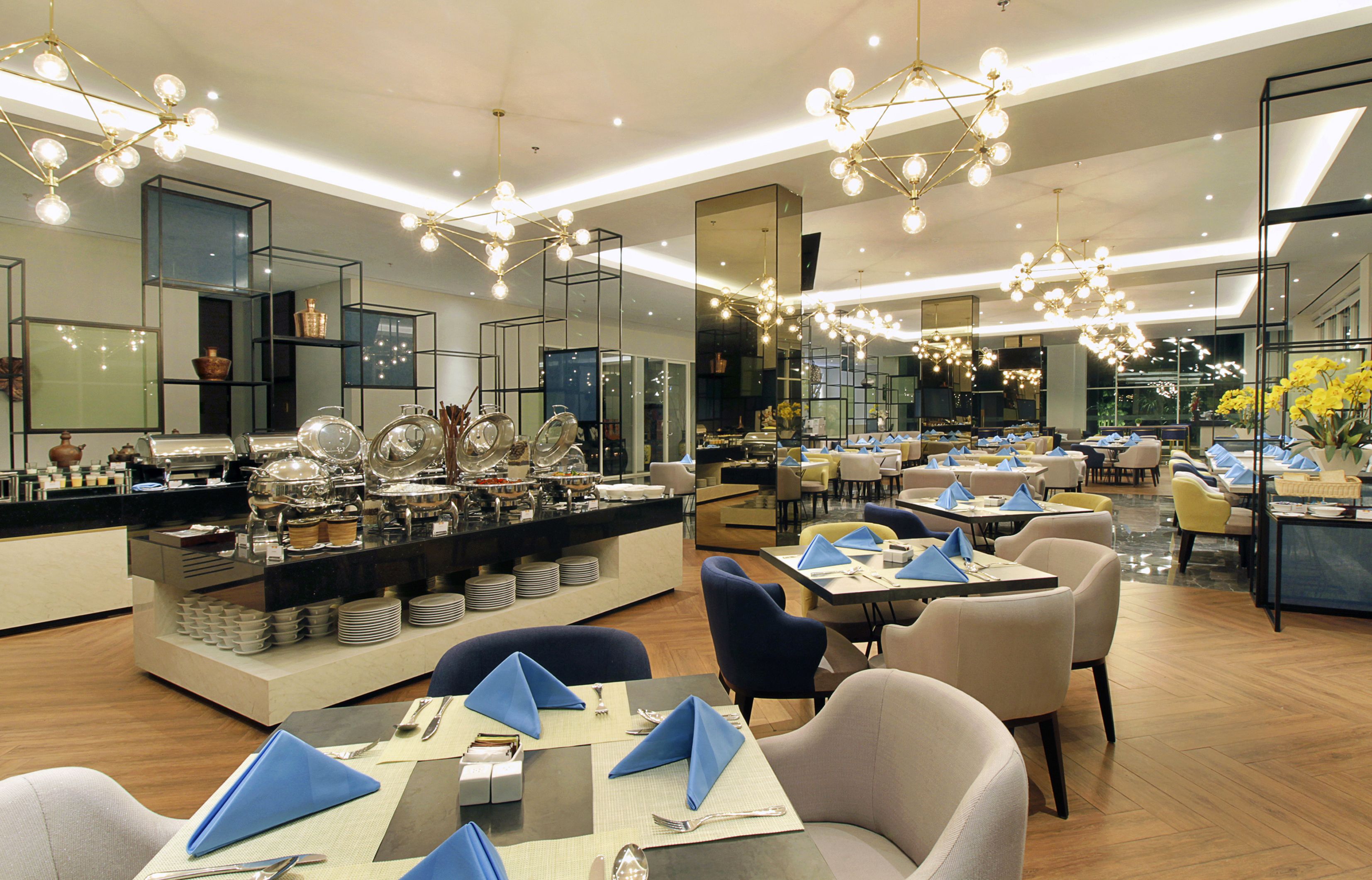 Un restaurante moderno con barra de buffet, varias zonas de estar e iluminación contemporánea.