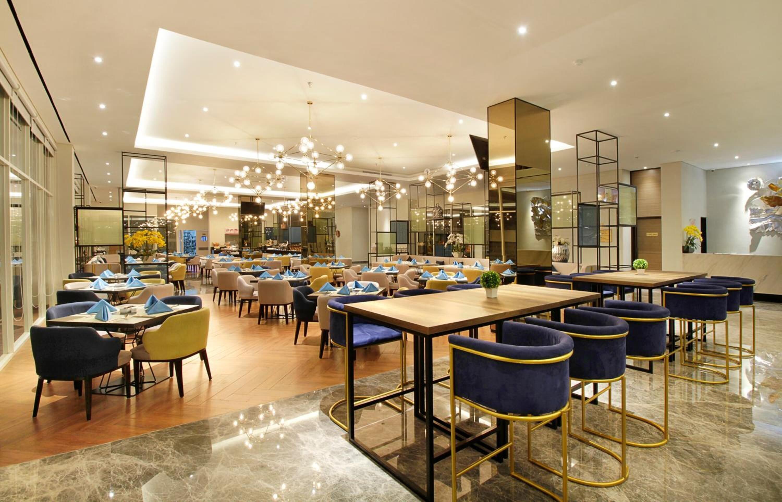 A spacious restaurant with multiple dining areas, including booths and bar seating, with a modern chandelier and reflective decor.