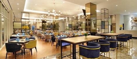 A spacious restaurant with multiple dining areas, including booths and bar seating, with a modern chandelier and reflective decor.