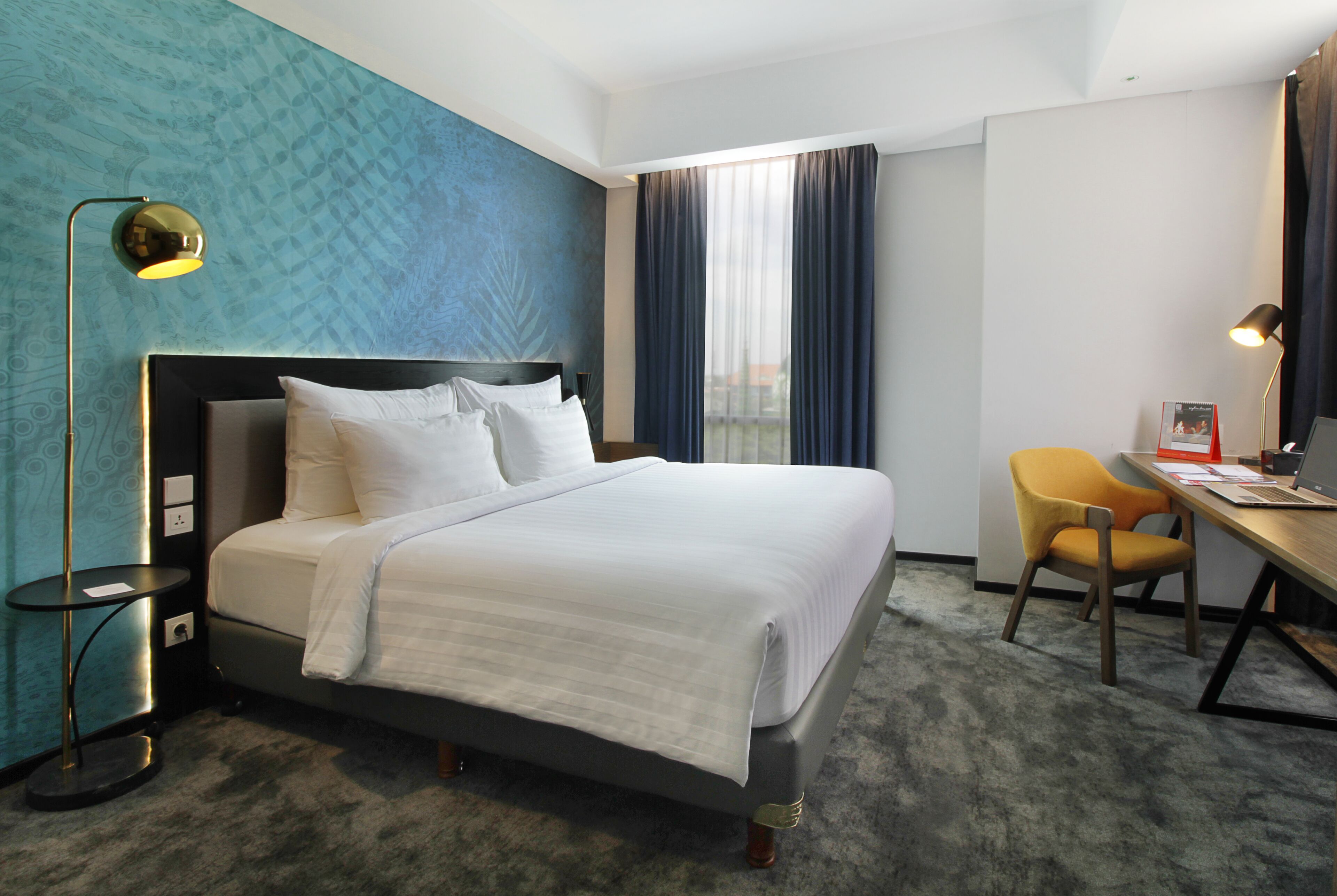 A hotel room with a bed, desk, chair, and a view of the city.