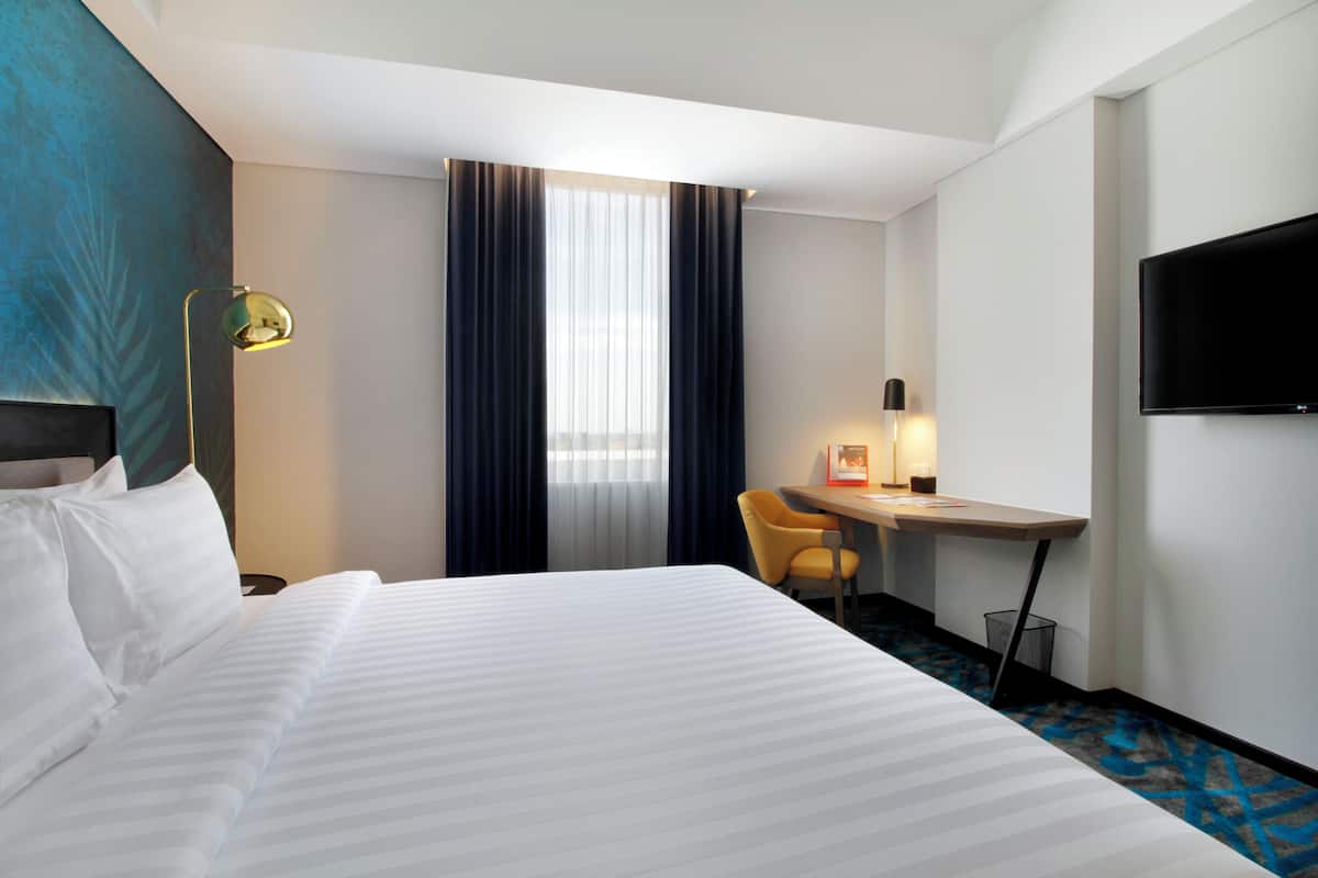 A hotel room with a large bed, a desk, a chair, a TV, and a window with curtains.