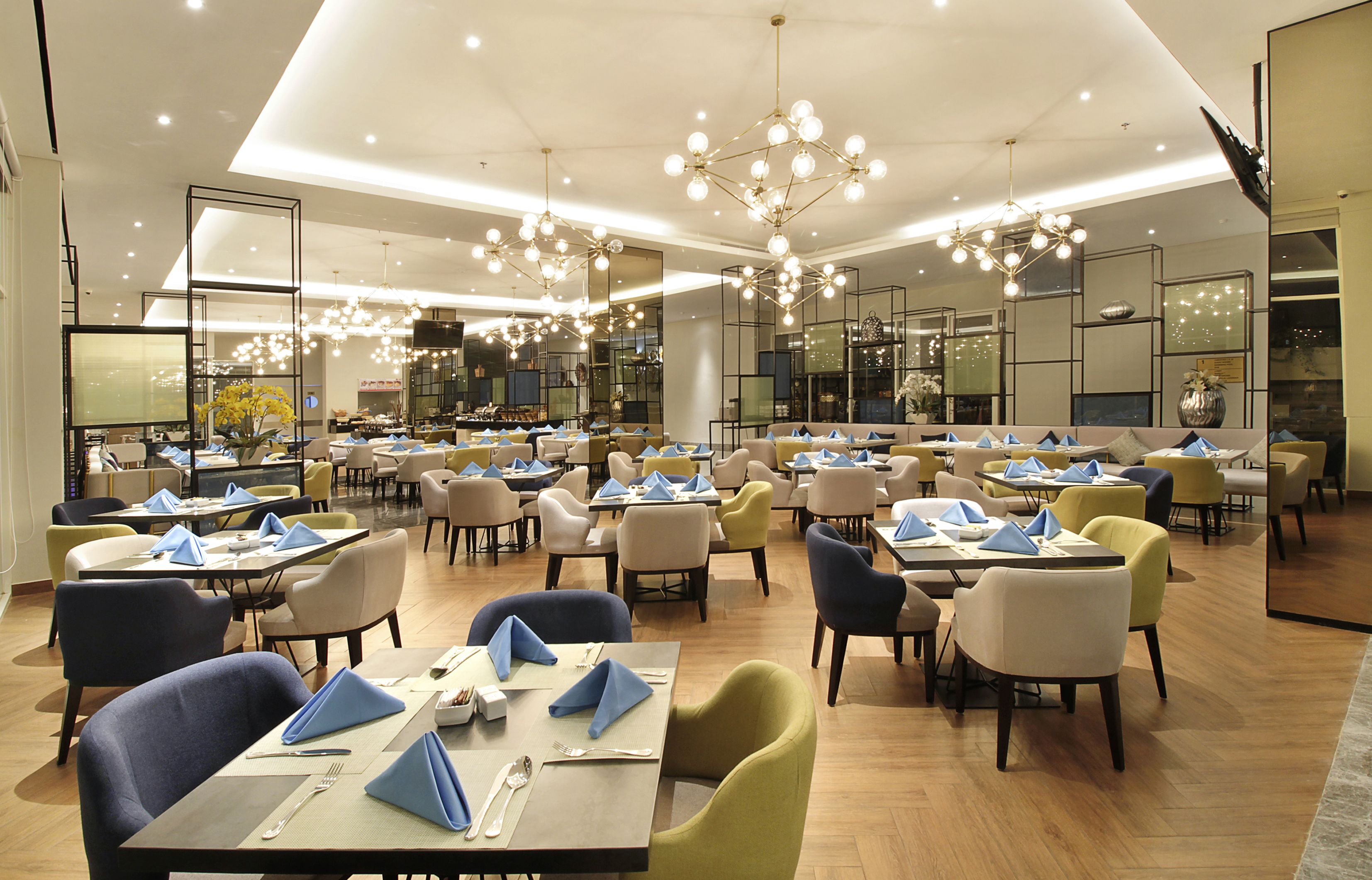 A spacious restaurant with multiple dining tables and chairs, modern lighting fixtures, and a clean, contemporary interior design.