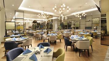 A spacious restaurant with multiple dining tables and chairs, modern lighting fixtures, and a clean, contemporary interior design.