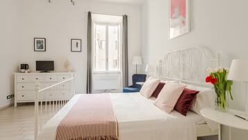 Una camera d'albergo con un letto, una scrivania, una sedia, un televisore e una finestra con tende.