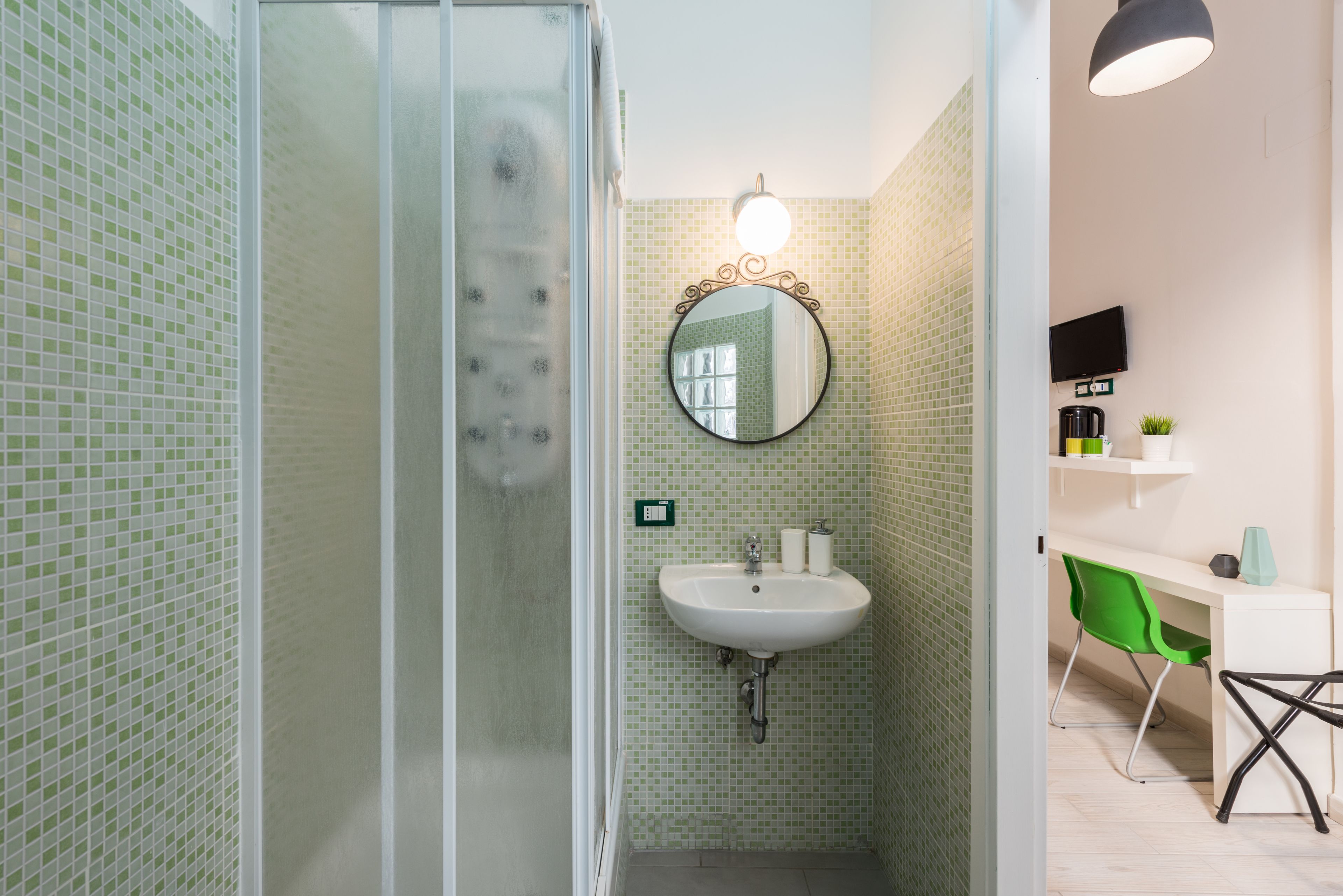 Un baño con cabina de ducha de vidrio, un lavabo con espejo y un escritorio con silla.