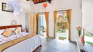 A bedroom with a bed, a ceiling fan, and a view of a garden through an open door. - Local Beach Homestay (Da Nang)