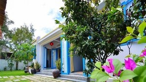 A house with a blue exterior, a front porch, and a garden with stepping stones and flowering plants. - Local Beach Homestay (Da Nang)
