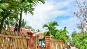 A wooden fence with a brick wall, a thatched-roof structure, and a paved path with a motorcycle parked nearby. - Local Beach Homestay (Da Nang)