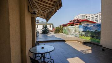 Un patio techado con mesa y sillas, piso de baldosas y vista a edificios al fondo.